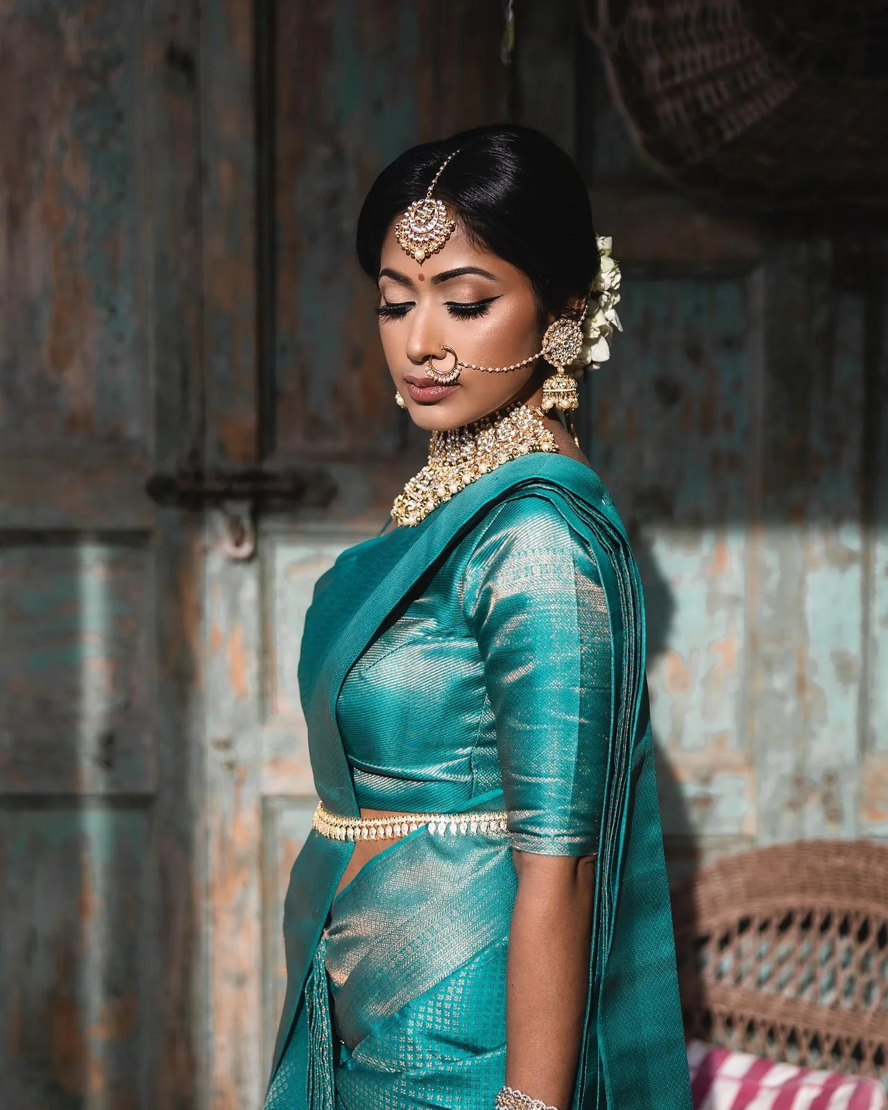 Bride in teal Kanjeevaram silk with antique gold temple jewellery, maang tikka and jasmine, in soft daylight.