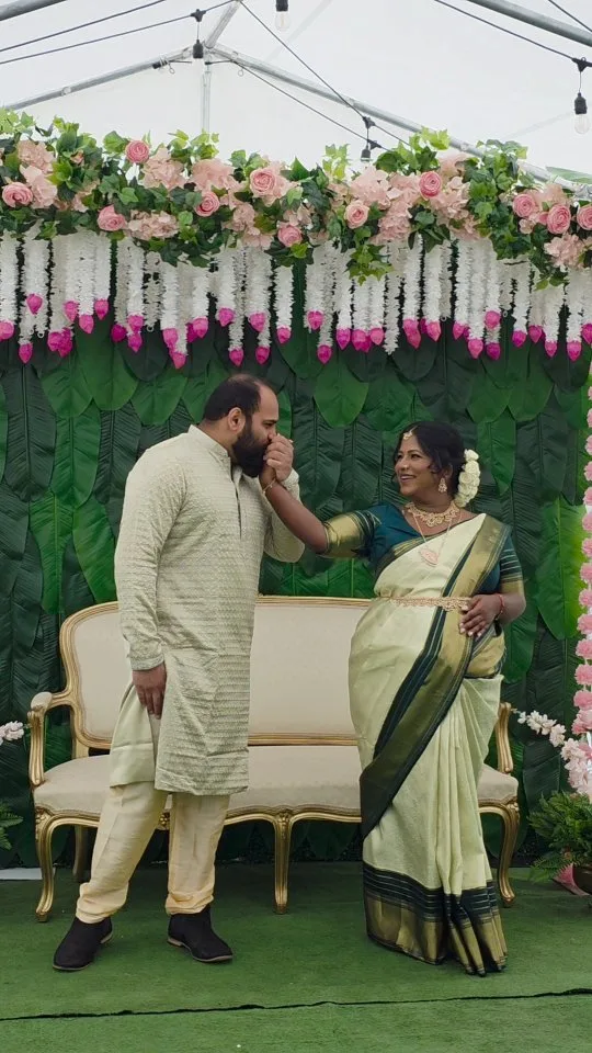 A couple on a rose and jasmine floral mandap stage — a wedding or engagement function styling.