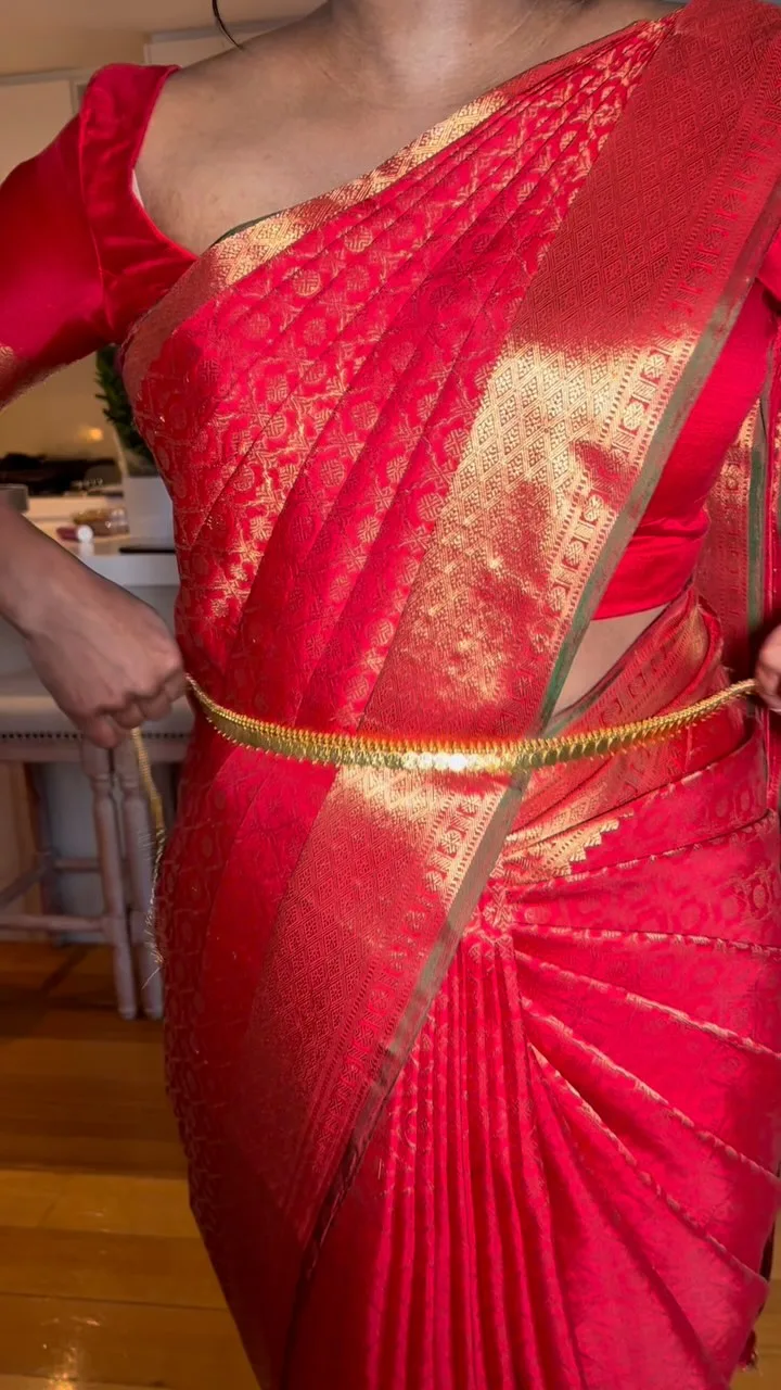 Close torso frame of a red Kanjeevaram silk drape set with an antique gold oddiyanam waist-belt, pleats pinned and placed.