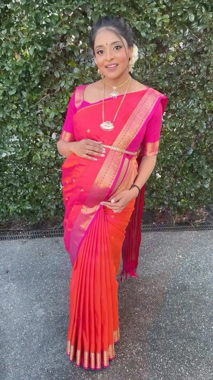 A woman in a pink and orange bicolour silk saree with gold waist-belt and jasmine, the drape showcasing the full pallu line.