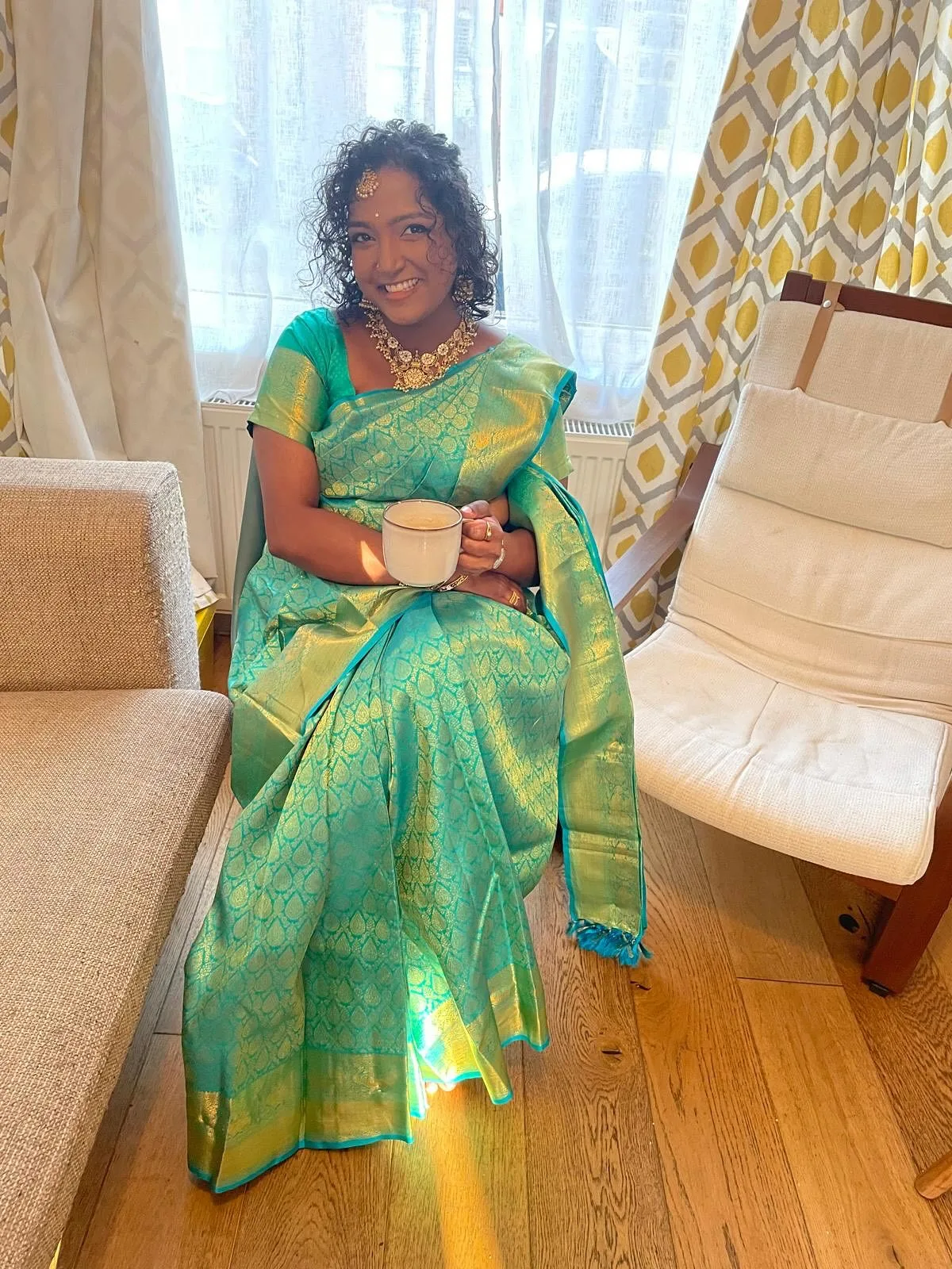 Woman in teal Kanjeevaram seated in a warm living room, a candid styling moment.